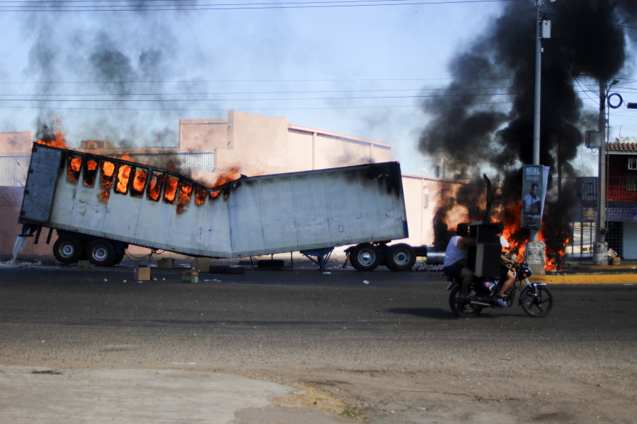 Men ride on a motorcycle past a burning truck on the streets of Culiacan, Sinaloa state, Thursday, Jan. 5, 2023. Mexican security forces have captured Ovidio Guzm?n, an alleged drug trafficker wanted by the United States and one of the sons of former Sinaloa cartel boss Joaqu?n "El Chapo" Guzm?n, in a pre-dawn operation outside Culiacan which has caused a wave of violence in the city.