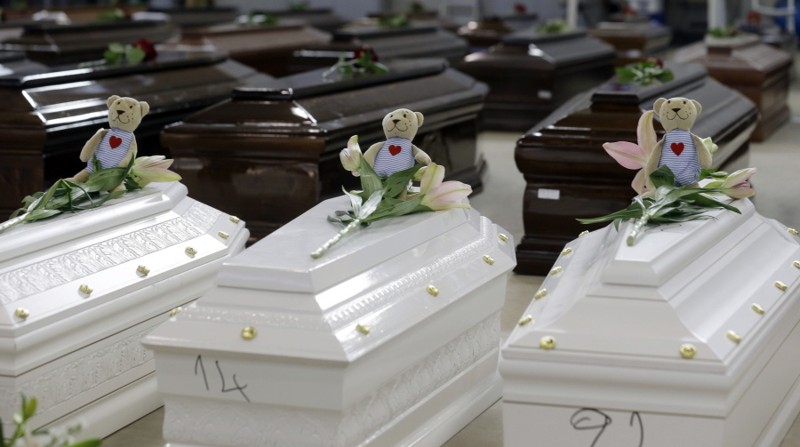 FILE - Teddy bears and flowers placed are placed on the coffins of deceased migrants inside a hangar at Lampedusa's airport, Italy, Saturday, Oct. 5, 2013. A decade ago this year, the head of the EU's executive branch, Jose Manuel Barroso stood visibly shaken before hundreds of coffins holding the corpses of migrants drowned off the Italian Island of Lampedusa.