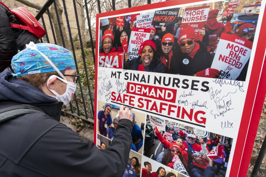FILE - Zach Clapp, a nurse in the Pediatric Cardiac ICU at Mount Sinai Hospital signs a board demanding safe staffing during a rally by NYSNA nurses from NY Presbyterian and Mount Sinai, Tuesday, March 16, 2021, in New York. Negotiations to keep 10,000 New York City nurses from walking off the job headed Friday, Jna. 6, 2023, into a final weekend as some major hospitals braced for a potential strike by sending ambulances elsewhere and transferring such patients as vulnerable newborns.