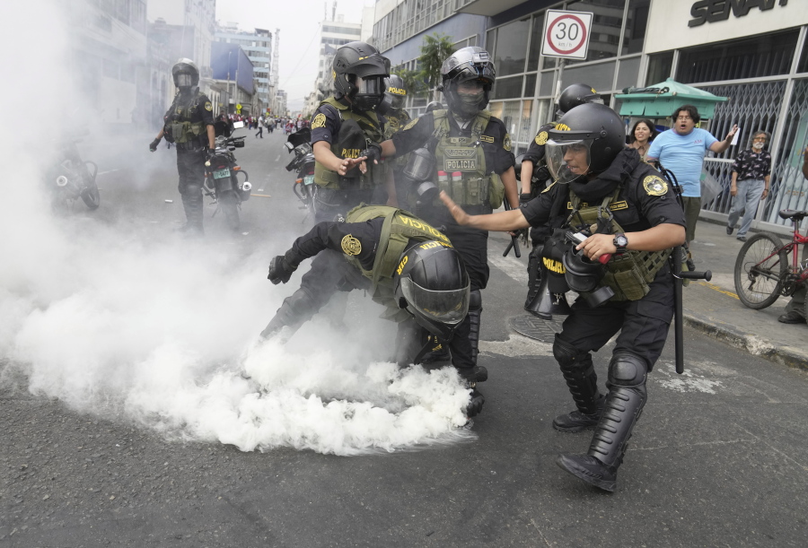 Police officers pick up a tear gas canister that was thrown back at them by anti-government protesters who traveled to the capital from across the country to march against Peruvian President Dina Boluarte in Lima, Peru, Wednesday, Jan. 18, 2023. Protesters are seeking immediate elections, Boluarte's resignation, the release of ousted President Pedro Castillo and justice for the dozens of protesters killed in clashes with police.