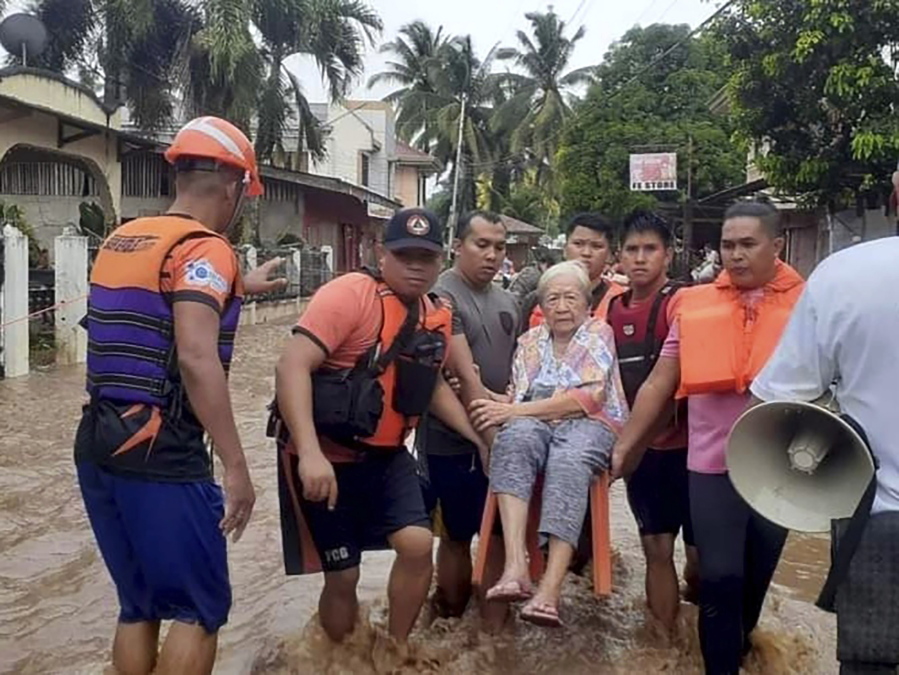 In this image provided by the Philippine Coast Guard, an elderly woman sits on a chair while being carried by coast guard personnel wading through floodwaters in Plaridel, Misamis Occidental province in the southern Philippines, Monday, Dec. 26, 2022. Heavy rains and floods devastated parts of the Philippines over the Christmas weekend.