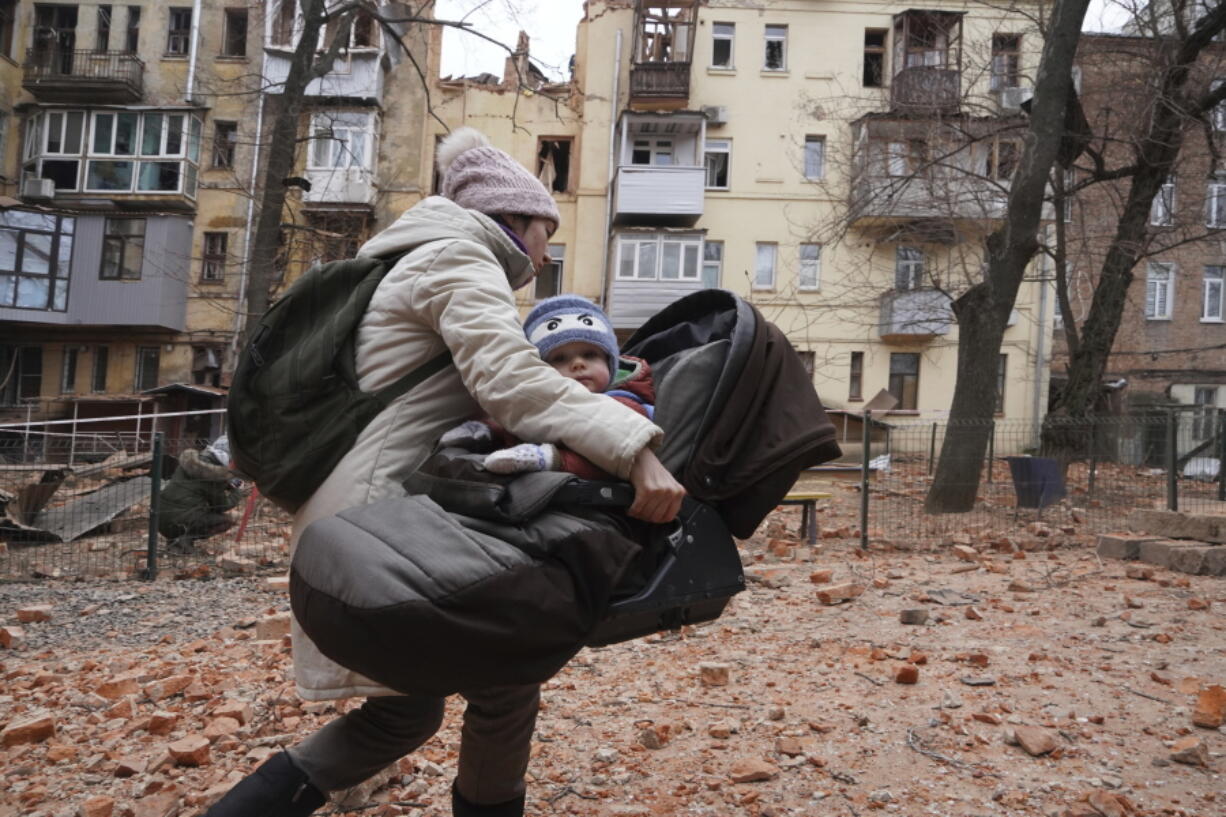 A woman carries her child as they evacuate from a residential building which was hit by a Russian rocket at the city center of Kharkiv, Ukraine, Monday, Jan. 30, 2023. Russian shelling killed at least five people and wounded 13 others during the previous 24 hours, Ukrainian authorities said Monday as the Kremlin's and Kyiv's forces remained locked in combat in eastern Ukraine.