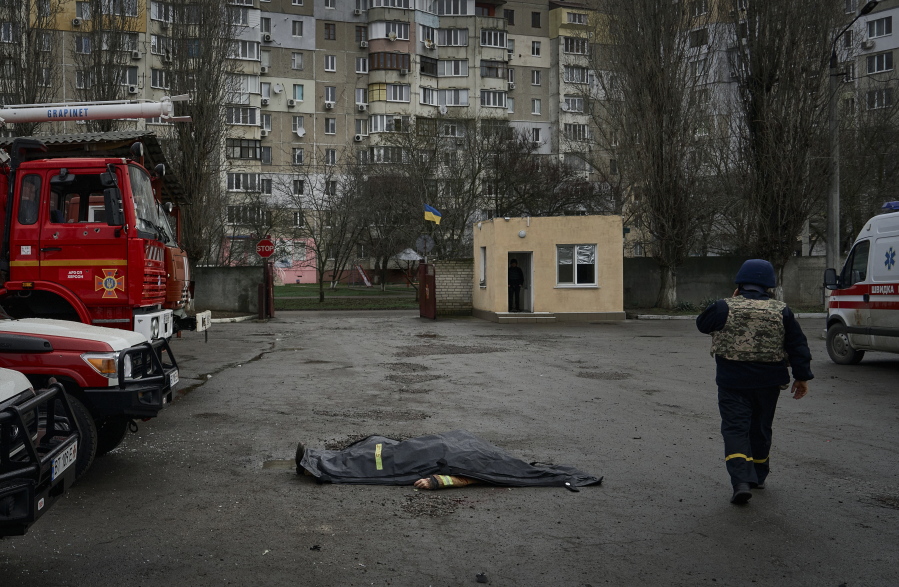 A firefighter passes by the dead body of a firefighter killed in the Russian shelling of the fire station in Kherson, Ukraine, on the Orthodox Christmas Eve Friday, Jan. 6, 2023.