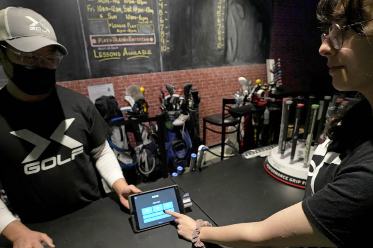 X-Golf manager J.W. Park, left, helps Ashley Moreno to check out at X-Golf indoor golf in Glenview, Ill., Friday, Jan. 20, 2023. Tipping fatigue, it seems, is swarming America as more businesses adopt digital payment methods that automatically prompts customers to leave a gratuity. (AP Photo/Nam Y.