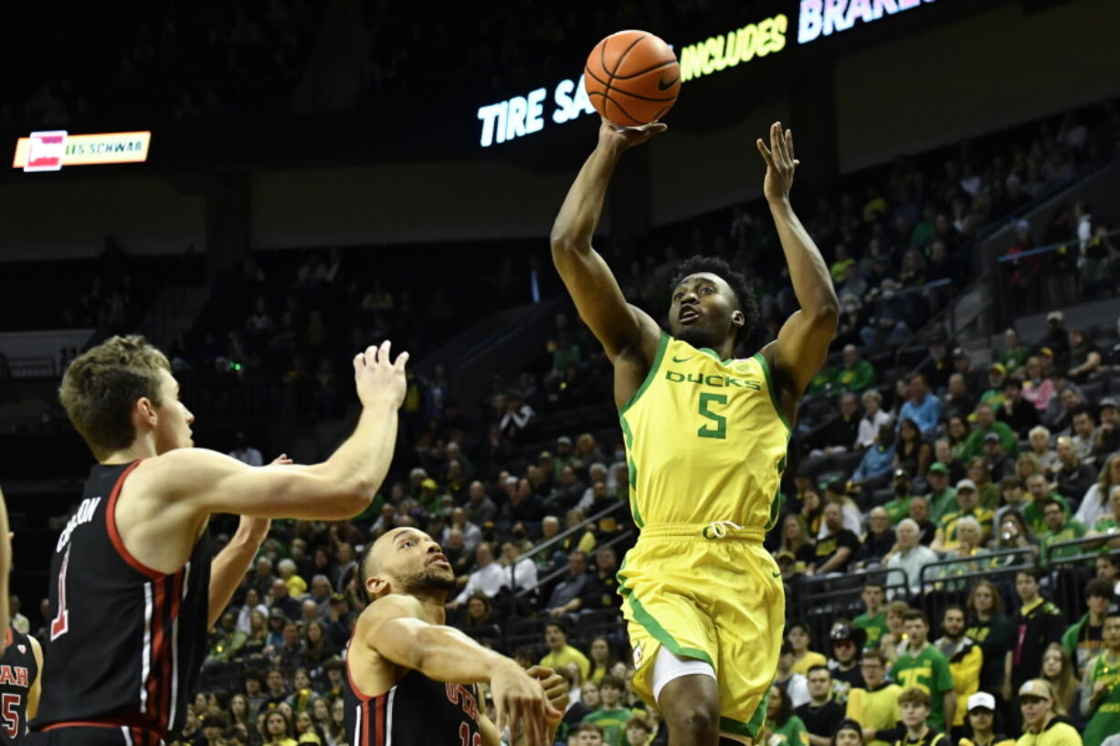 Oregon guard Jermaine Couisnard (5) looks to shoot over Utah forward Ben Carlson, left, and guard Marco Anthony, center, during the first half of an NCAA college basketball game Saturday, Jan. 28, 2023, in Eugene, Ore.