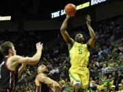 Oregon guard Jermaine Couisnard (5) looks to shoot over Utah forward Ben Carlson, left, and guard Marco Anthony, center, during the first half of an NCAA college basketball game Saturday, Jan. 28, 2023, in Eugene, Ore.