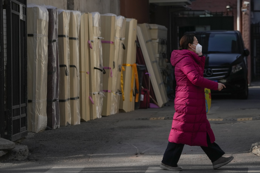 A woman wearing a face mask walks by empty coffins placed at a mortuary of a hospital in Beijing, Friday, Jan. 6, 2023.