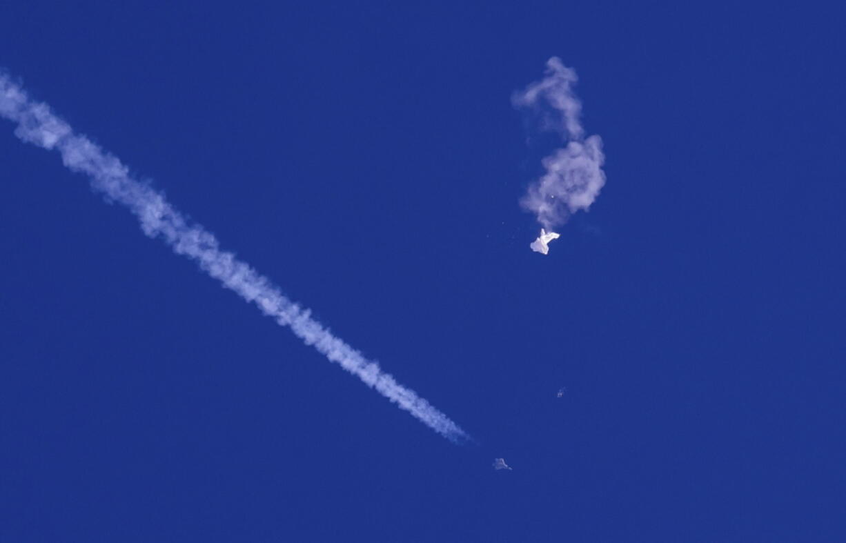 In this photo provided by Chad Fish, the remnants of a large balloon drift above the Atlantic Ocean, just off the coast of South Carolina, with a fighter jet and its contrail seen below it, Saturday, Feb. 4, 2023. The downing of the suspected Chinese spy balloon by a missile from an F-22 fighter jet created a spectacle over one of the state's tourism hubs and drew crowds reacting with a mixture of bewildered gazing, distress and cheering.