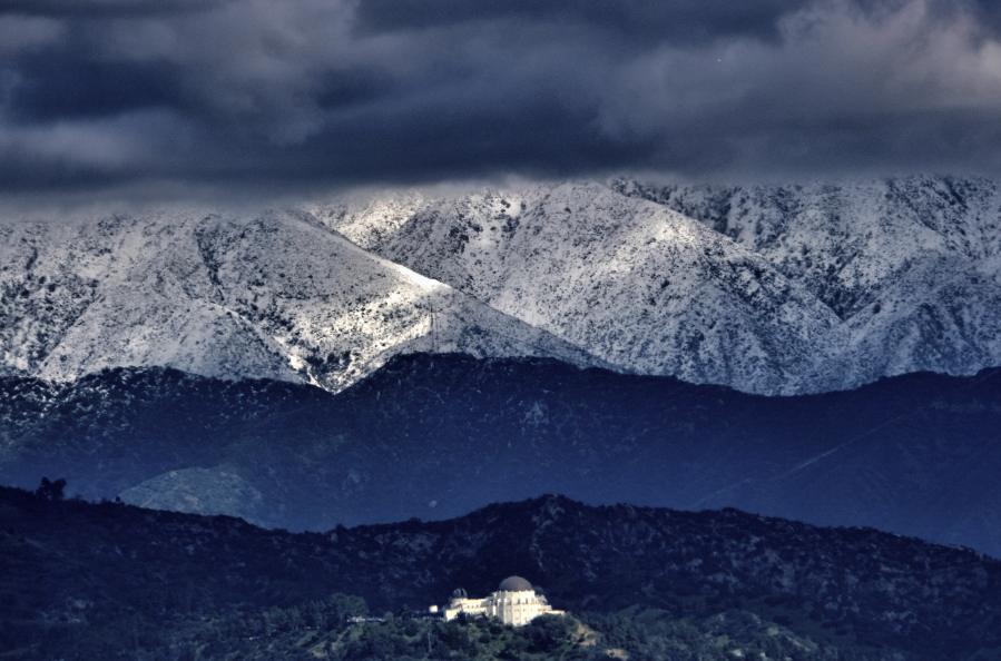 Storm clouds and snow are seen over the San Gabriel mountain range behind Griffith Observatory in the Hollywood Hills part of Los Angeles on Sunday, Feb. 26, 2023. A powerful winter storm that swept the West Coast with flooding and frigid temperatures has shifted to southern California, swelling rivers to dangerous levels and dropping snow in even low-lying areas around Los Angeles.