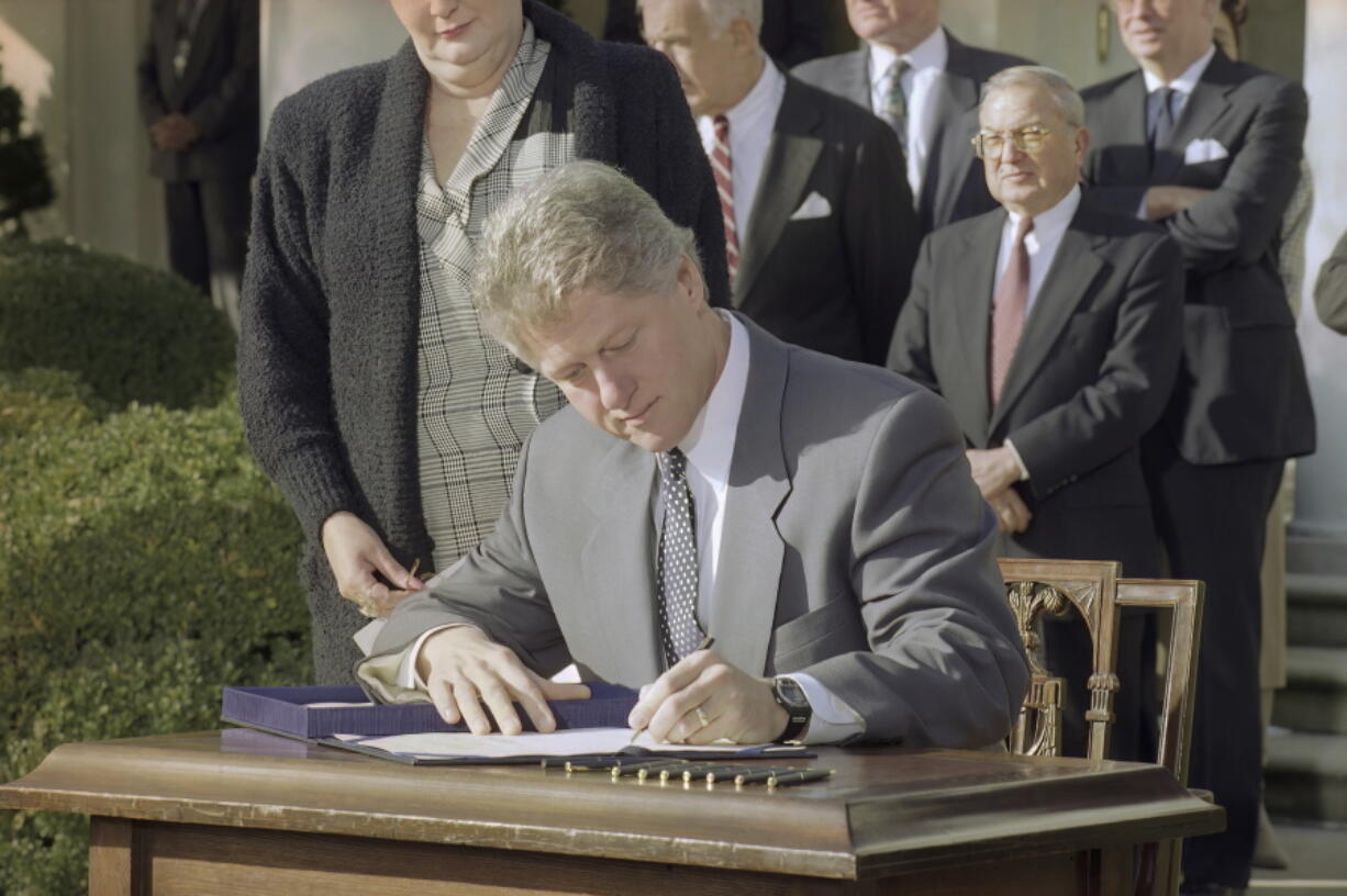 FILE - President Bill Clinton reaches for a pen as he signs the Family Leave Bill into law during a ceremony in the Rose Garden in Washington, Feb. 5, 1993. Looking over Clinton's shoulder is Vicki Yandle of Marietta, Ga., whose husband lost his job when he took off to take care of their sick daughter. Behind the President are House Speaker Tom Foley of Wash., Sen. Ted Kennedy, D-Mass., and Rep. William Ford, D-Mich. President Joe Biden is playing host to former President Bill Clinton to mark the 30th anniversary of the Family and Medical Leave Act. It was the first piece of legislation that Clinton signed into law after taking office in 1993.