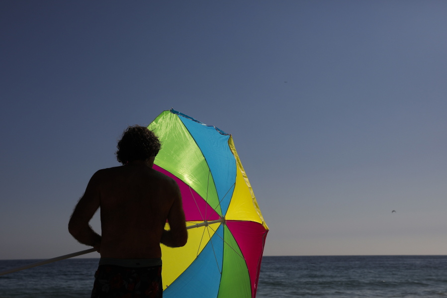 FILE - A man folds his umbrella on the beach Tuesday, Aug. 7, 2018, in Laguna Beach, Calif. Environmental advocates are celebrating in Laguna Beach -- but it won't be with balloons. The hilly, seaside city is weighing a plan to ban the sale and public use of balloons to curtail the risk of devastating wildfires and eliminate a major source of trash floating near the community's scenic shores. (AP Photo/Jae C.