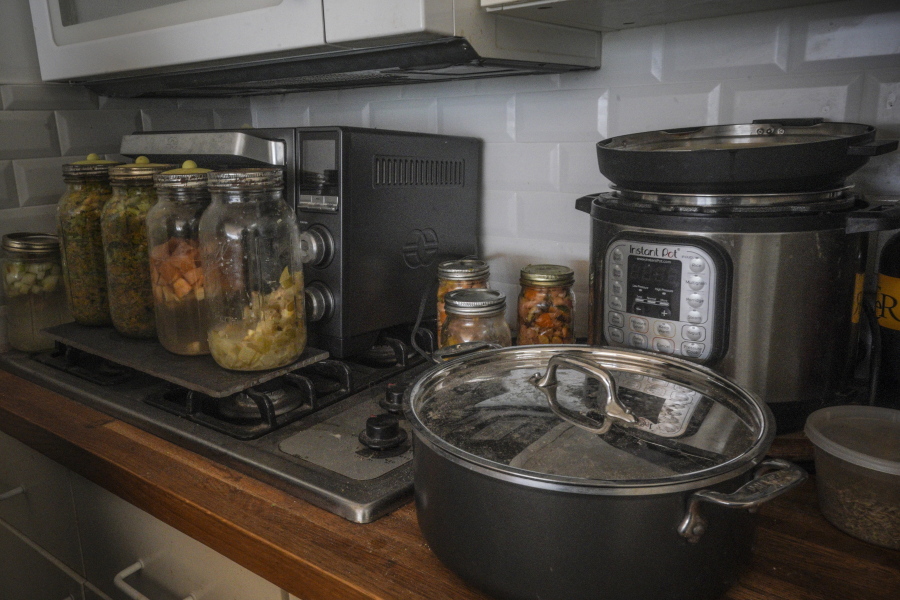 Jars of fermenting fruits and vegetables, left, sit on top of a retired gas stove replaced by an electric cooker, right, in Josh Spodek's Greenwich Village apartment kitchen, Tuesday Jan. 24, 2023, in New York.