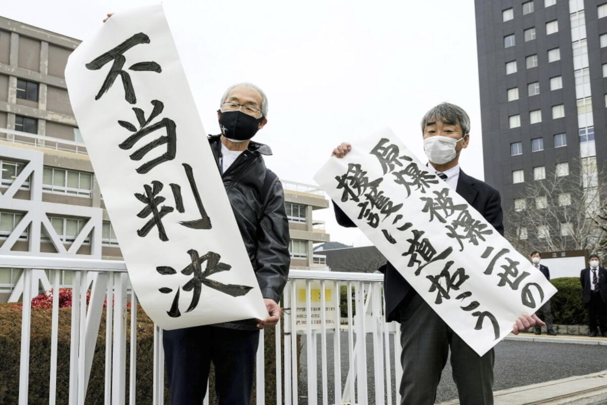 Plaintiff Katsuhiro Hirano, right, and unidentified lawyer for the plaintiffs display signs after a judgement at Hiroshima District Court in Hiroshima, western Japan Tuesday, Feb. 7, 2023.