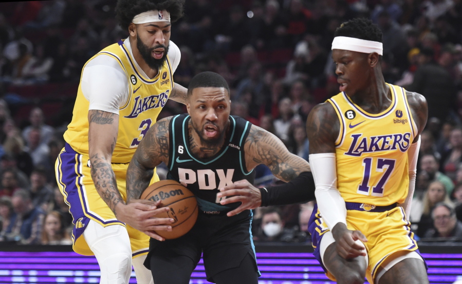 Portland Trail Blazers guard Damian Lillard, center, drives to the basket against Los Angeles Lakers forward Anthony Davis, left, and guard Dennis Schroder, right, during the first half of an NBA basketball game in Portland, Ore., Monday, Feb. 13, 2023.