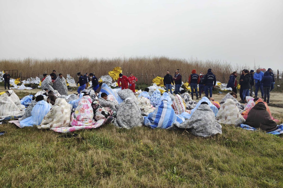 Rescued migrants sit covered in blankets at a beach near Cutro, southern Italy, Sunday, Feb. 26, 2023. Rescue officials say an undetermined number of migrants have died and dozens have been rescued after their boat broke apart off southern Italy.