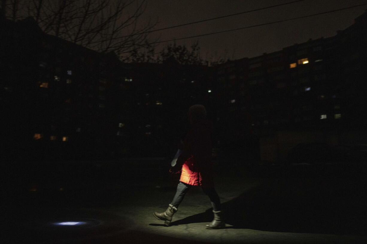 A woman lights up the road with a flashlight during blackout in Kyiv, Ukraine, Friday, Feb. 3, 2023.