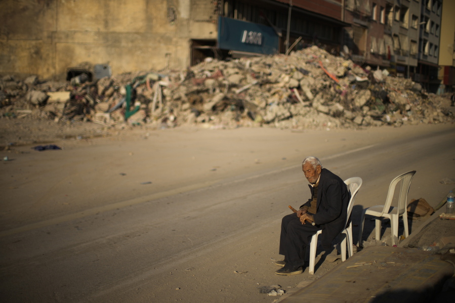 A man sits on a chair next to rubble of a destroyed building in Iskenderun city, southern Turkey, Tuesday, Feb. 14, 2023. Thousands left homeless by a massive earthquake that struck Turkey and Syria a week ago packed into crowded tents or lined up in the streets for hot meals as the desperate search for survivors entered what was likely its last hours.