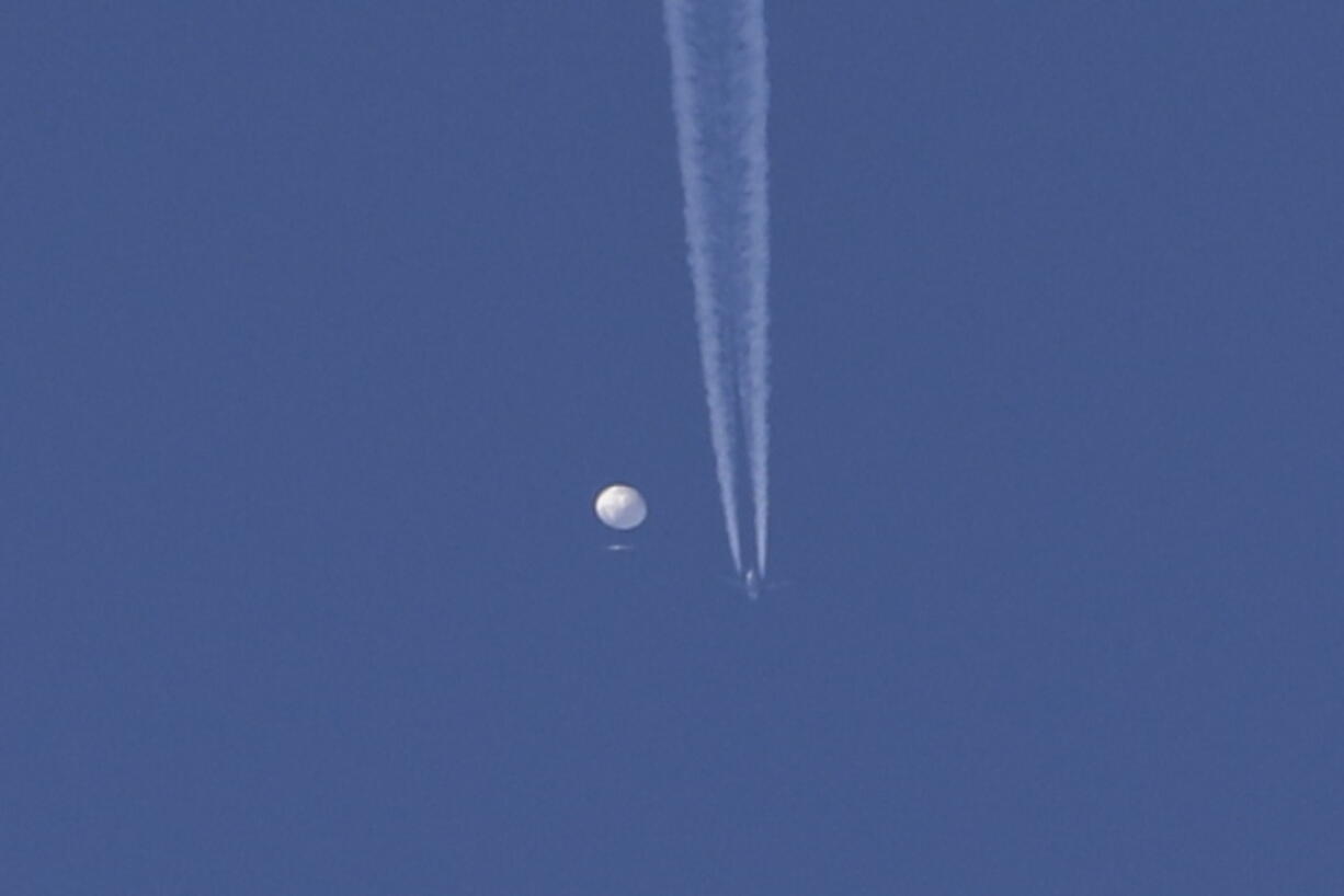 In this photo provided by Brian Branch, a large balloon drifts above the Kingstown, N.C. area, with an airplane and its contrail seen below it. The United States says it is a Chinese spy balloon moving east over America at an altitude of about 60,000 feet (18,600 meters), but China insists the balloon is just an errant civilian airship used mainly for meteorological research that went off course due to winds and has only limited "self-steering" capabilities.