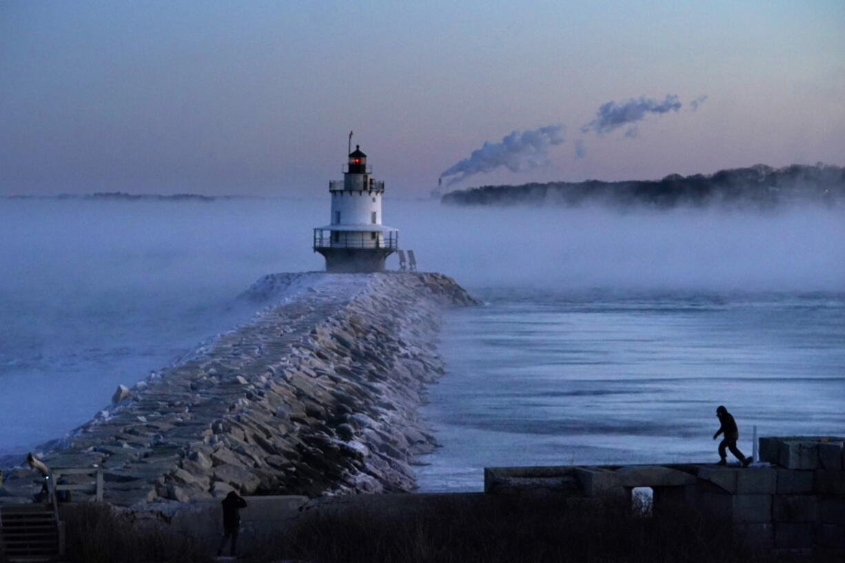 A man walks on sea wall near Spring Point Ledge Light, Saturday, Feb. 4, 2023, in South Portland, Maine. The morning temperature was about -10 degrees Fahrenheit. (AP Photo/Robert F.
