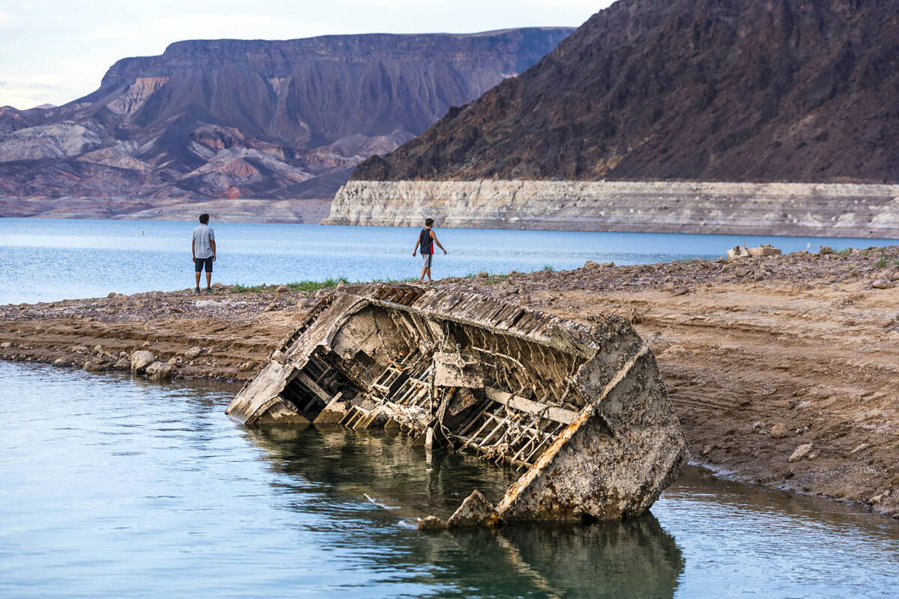 Hikers pass a previously sunken World War II-era Higgins landing craft that once was 185 feet below the surface is nearly on the shoreline as waters keep receding on July 26, 2022, near Boulder City, Nevada. (L.E.