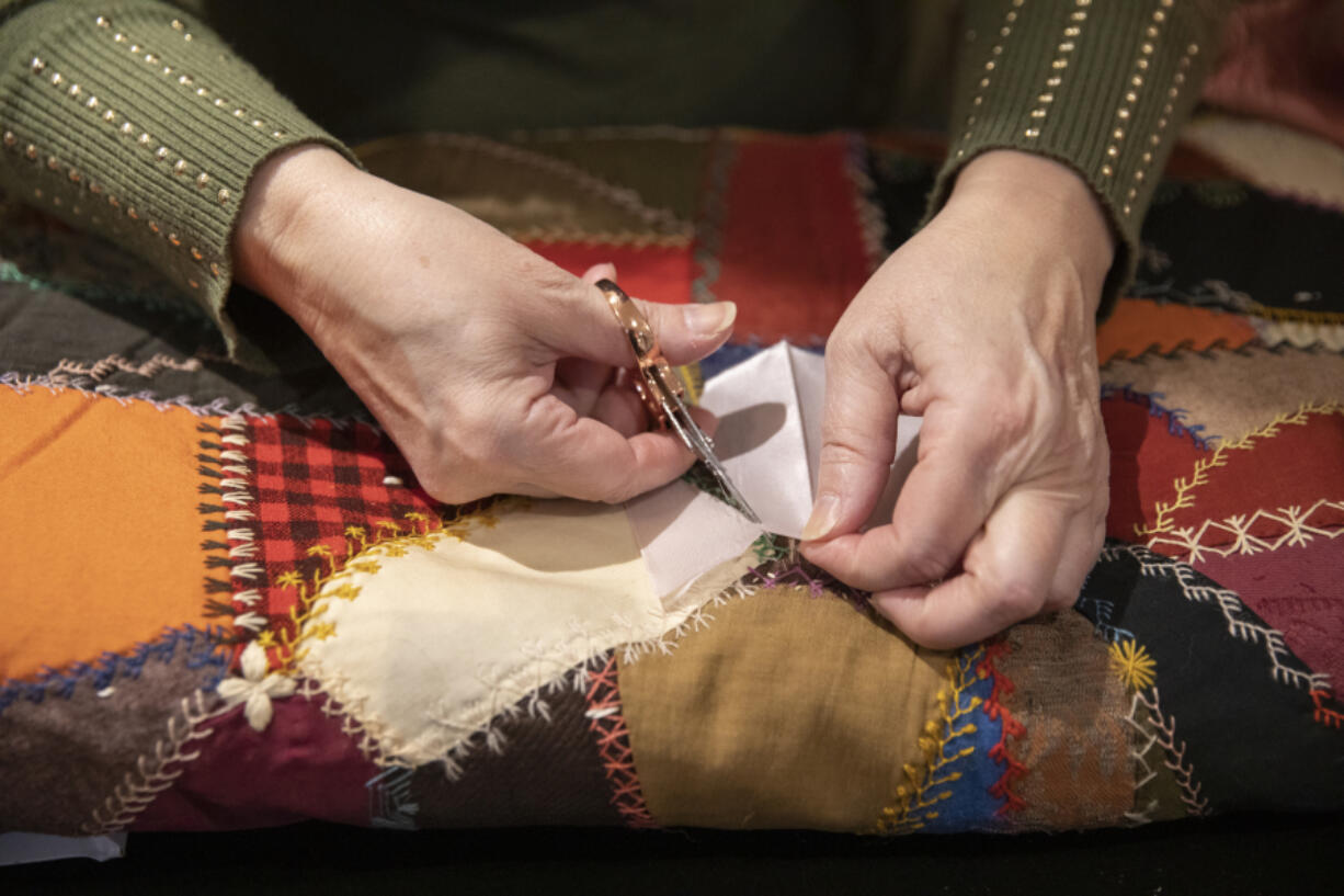 Miki Landis cuts a piece of silk fabric to mend a frayed section of quilt at her shop, The Enchanted Rose Emporium, located inside Providence Academy in Vancouver.