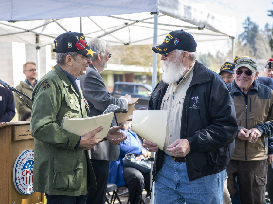 Vietnam veteran Patrick Locke, left, hands out commemorative pins and papers to other veterans before the Witness Tree dedication at Clark College.