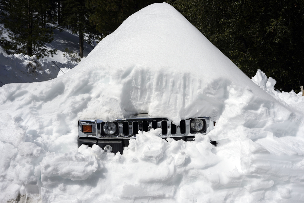 A vehicle's grill sticks out of a snow mound after a series of storms, Wednesday, March 8, 2023, in Lake Arrowhead, Calif.