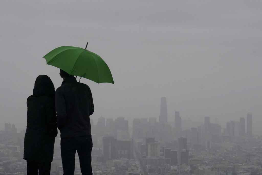 People stand under an umbrella while looking toward the skyline from Twin Peaks in San Francisco, Thursday, March 9, 2023. California is bracing for the arrival of an atmospheric river that forecasters warn will bring heavy rain, strong winds, thunderstorms and the threat of flooding even as the state is still digging out from earlier storms.