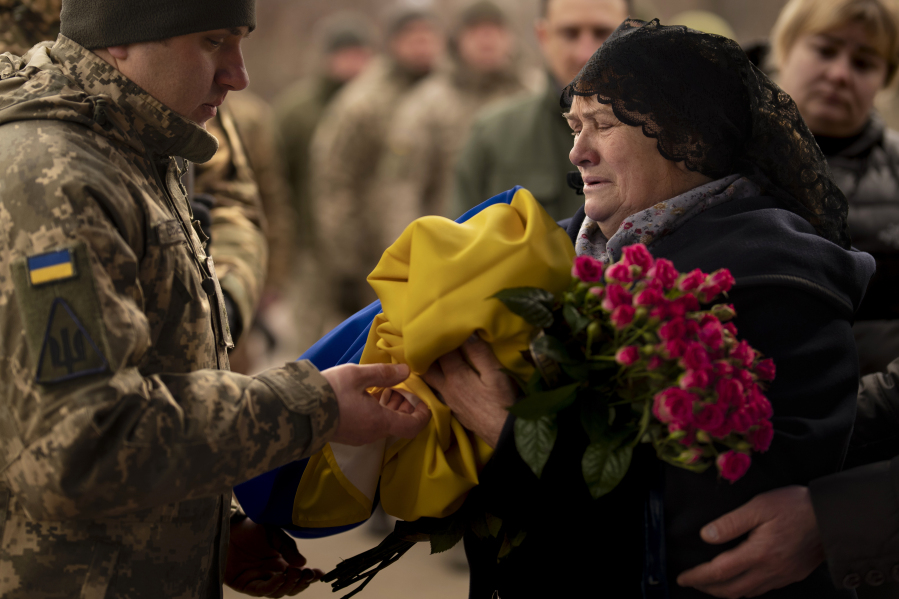 Tetiana Hurieieva, the mother of Volodymyr Hurieiev, a Ukrainian soldier killed in the Bakhmut area, receives the flag that draped his coffin, during the funeral in Boryspil, Ukraine, Saturday, March 4, 2023. Pressure from Russian forces mounted Saturday on Ukrainians hunkered down in Bakhmut, as residents attempted to flee with help from troops who Western analysts say may be preparing to withdraw from the key eastern stronghold.