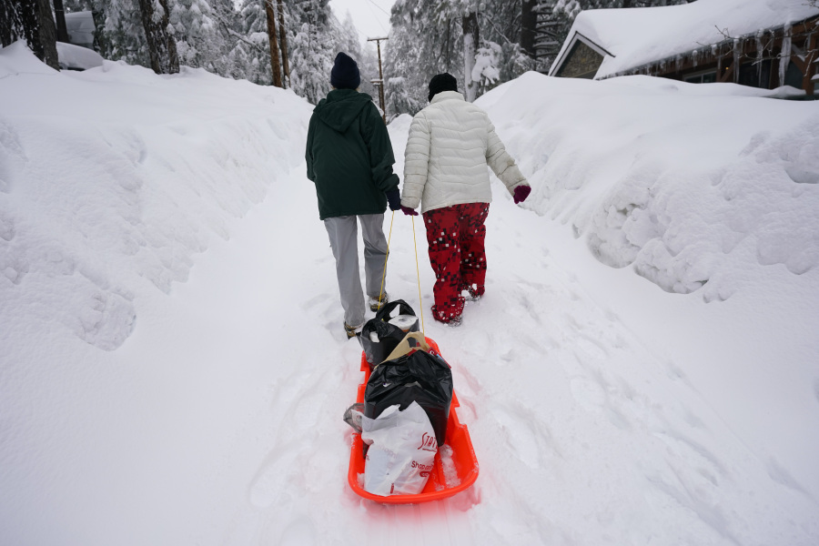 Angie Gourirand, left, and Cindy Maner, whose cars are buried in the snow, carry their groceries on a sled in Running Springs, Calif., Tuesday, Feb. 28, 2023. Beleaguered Californians got hit again Tuesday as a new winter storm moved into the already drenched and snow-plastered state, with blizzard warnings blanketing the Sierra Nevada and forecasters warning residents that any travel was dangerous. (AP Photo/Jae C.