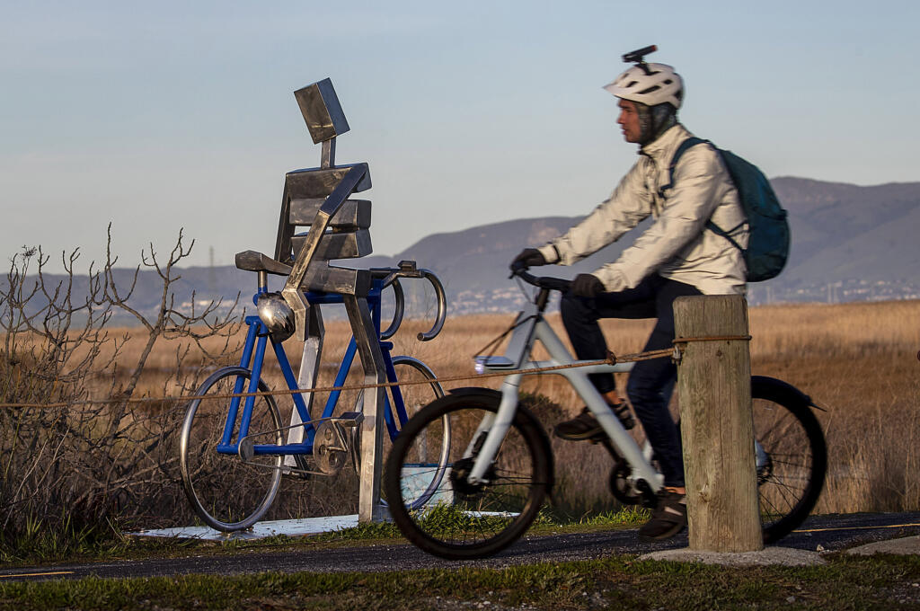 Art reflects reality as an e-bike bicyclist rides the Renzel Trail, a legal trail for e-bikes to use, through the Baylands past a metallic cyclist sculpture by James Moore in Palo Alto, California, on March 1, 2023.