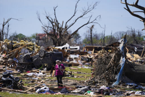 FILE - A woman walks near an uprooted tree, a flipped vehicle and debris from homes damaged by a tornado, Monday, March 27, 2023, in Rolling Fork, Miss. President Joe Biden on Friday will visit a Mississippi town ravaged by a deadly tornado even as a new series of severe storms threatens to rip across the Midwest and South.