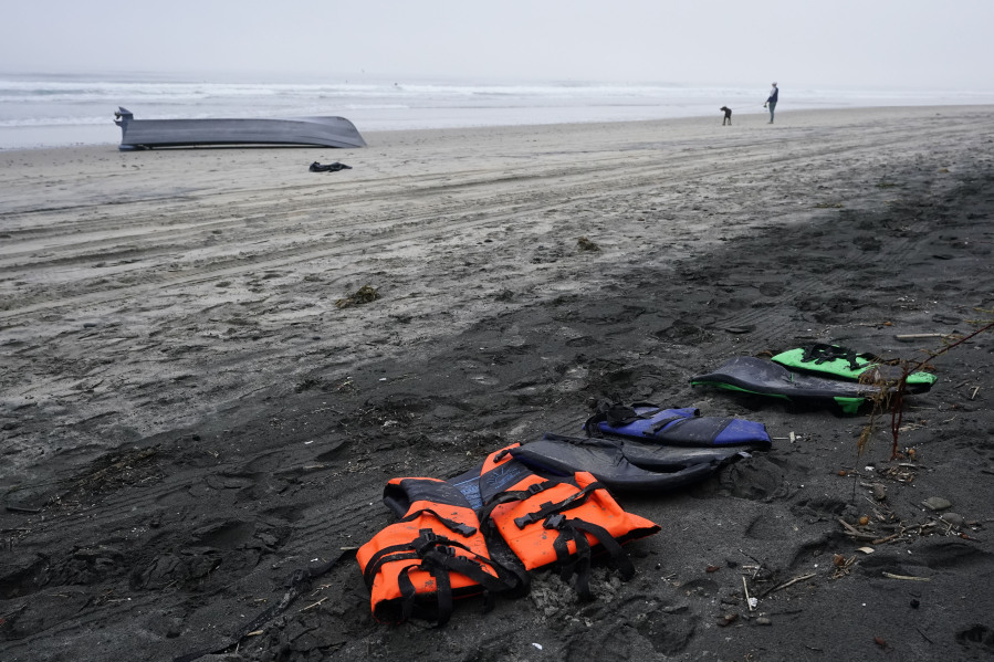 A boat sits overturned near a row of life jackets on Blacks Beach, Sunday, March 12, 2023, in San Diego. Authorities say multiple people were killed when two suspected smuggling boats overturned off the coast San Diego, and crews were searching for additional victims.