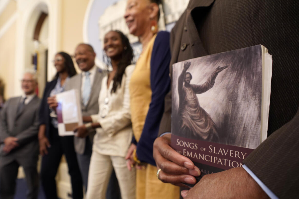 FILE -- Dr. Amos C. Brown, Jr., vice chair for the California Reparations Task Force, right, holds a copy of the book Songs of Slavery and Emancipation, as he and other members of the task force pose for photos at the Capitol in Sacramento, Calif., on June 16, 2022. Economists for a California reparations task force estimate the state owes Black residents at least $800 billion for harms in policing, housing and health. The preliminary estimate will be discussed at the Wednesday, March 29, 2023, meeting of the state reparations task force.