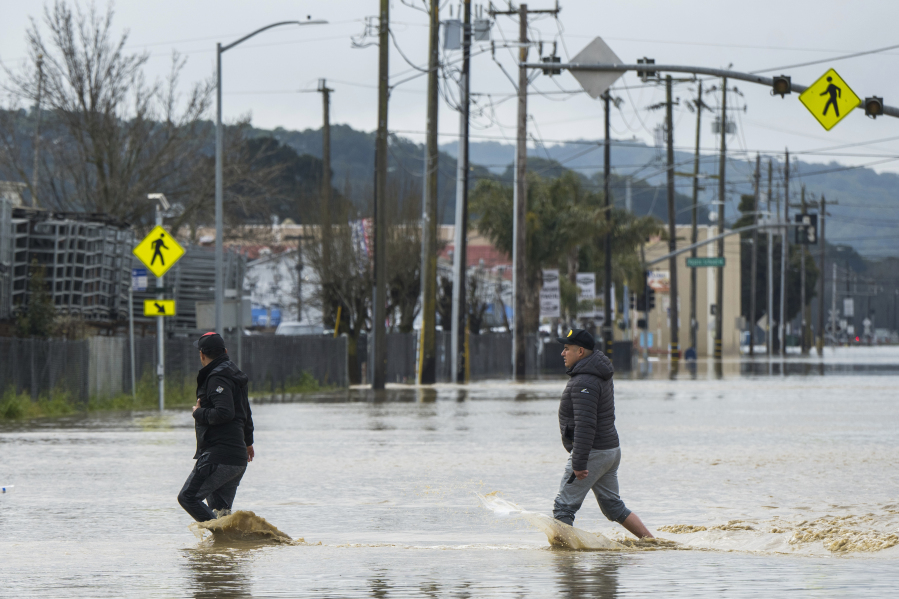 People walk through floodwaters in Watsonville, Calif., Saturday, March 11, 2023.  Gov. Gavin Newsom has declared emergencies in 34 counties in recent weeks, and the Biden administration approved a presidential disaster declaration for some on Friday morning, a move that will bring more federal assistance.