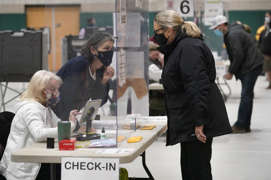 FILE - A poll worker, center left, speaks through a plastic barrier while assisting a voter in a polling station at Marshfield High School, Nov. 3, 2020, in Marshfield, Mass. A bipartisan effort among states to combat voter fraud has found itself in the crosshairs of conspiracy theories fueled by Donald Trump's false claims about the 2020 presidential election and now faces an uncertain future.