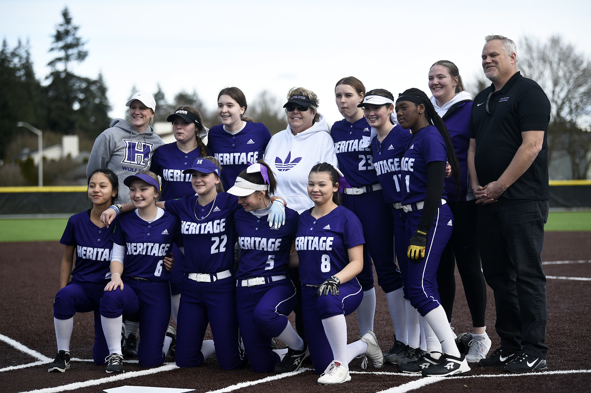 The Heritage softball team poses for a photo with former athletic director Leta Meyer (center in white) and principal Derek Garrison, right, prior to the Timberwolves' 8-1 win over Kelso in a softball game at Heritage on Tuesday, March 14, 2023.
