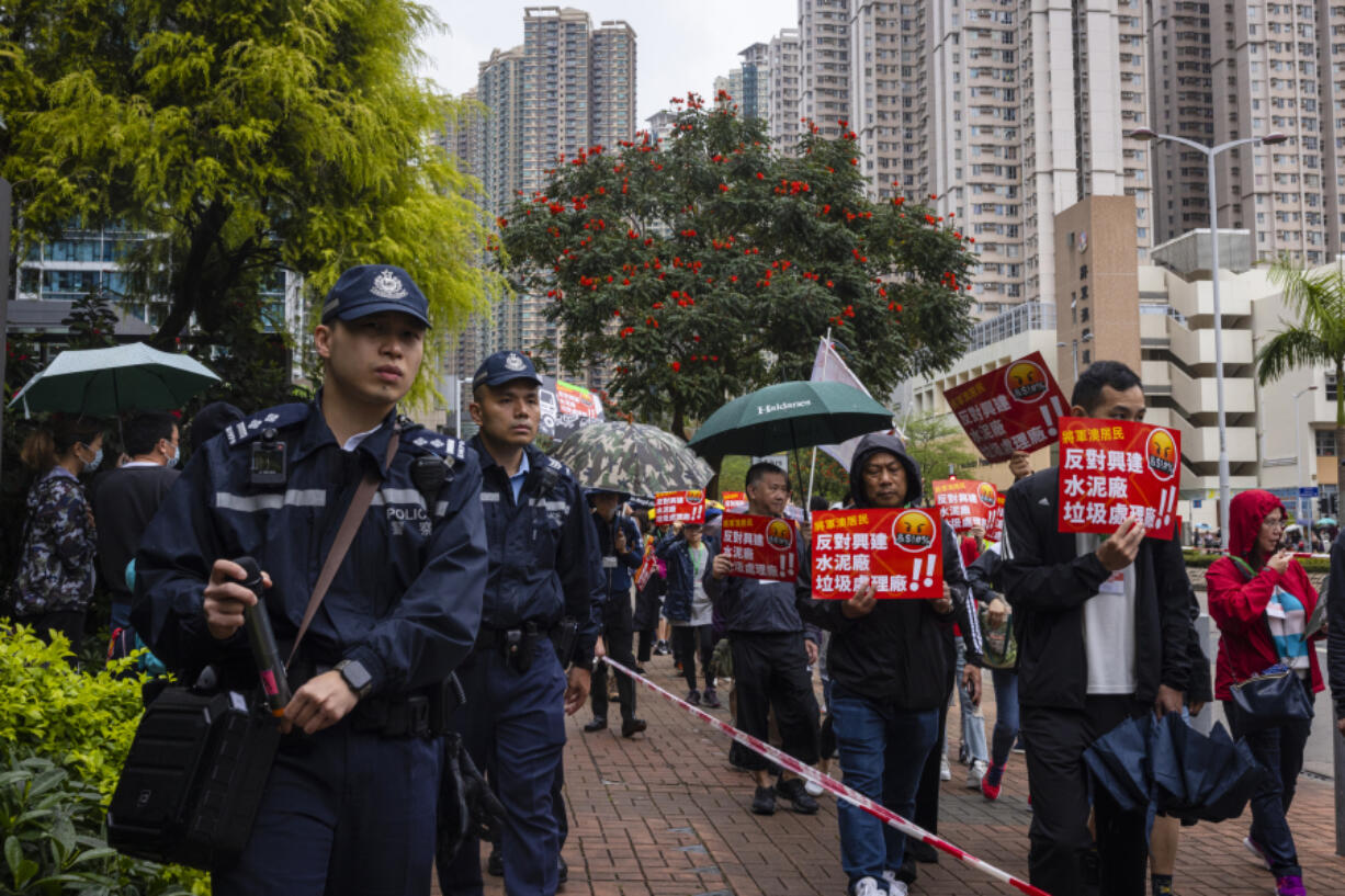 Police watch protesters walking within a cordon line wearing number tags during a rally in Hong Kong, Sunday, March 26, 2023. Dozens of people on Sunday joined Hong Kong's first authorized demonstration against the government since the lifting of major COVID-19 restrictions under unprecedentedly strict rules, including wearing a numbered badge around their necks.