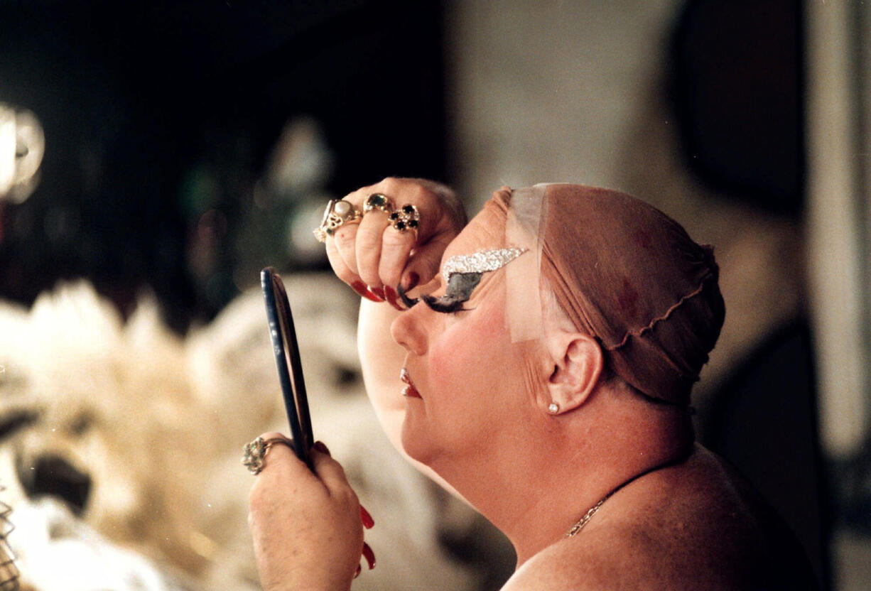 FILE - Walter C. Cole delicately attaches his eyelashes in the basement dressing room of his club in Portland, Ore., on Dec. 9, 1998, as the transformation to Darcelle takes shape.  Cole, better known as the iconic drag queen who performed for decades as Darcelle, has died of natural causes in Portland, Ore, on Thursday, March 24, 2023. (.