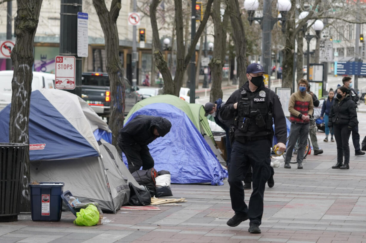 FILE - A Seattle police officer walks past tents used by people experiencing homelessness, March 11, 2022, during the clearing and removal an encampment in Westlake Park in downtown Seattle. The U.S. Justice Department and Seattle officials on Tuesday, March 28, 2023, asked a judge to end most federal oversight of the city's police department, saying its sustained, decade-long reform efforts are a model for cities around the country whose law enforcement agencies face federal civil rights investigations. (AP Photo/Ted S.
