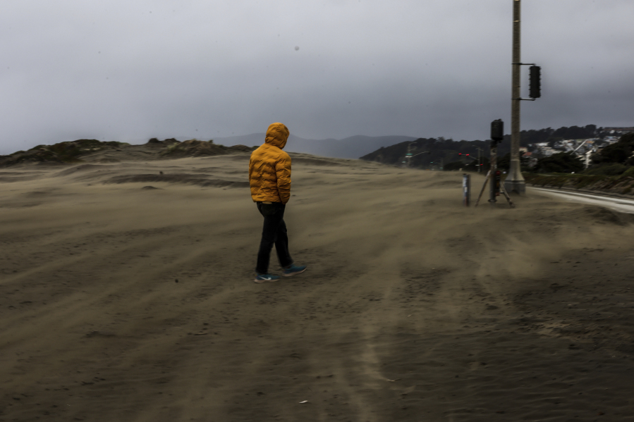 A man walks through a windstorm at Ocean Beach on a stormy morning in San Francisco on Tuesday, March 14, 2023.