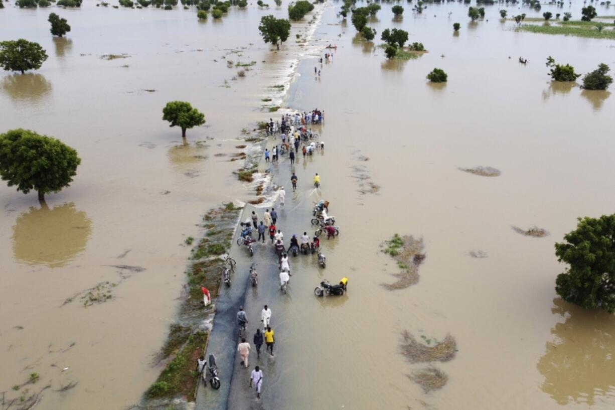 FILE - People walk through floodwaters after heavy rainfall in Hadeja, Nigeria, Sept 19, 2022. Publication of a major new United Nations report on climate change is being held up by a battle between rich and developing countries over emissions targets and financial aid to vulnerable nations.