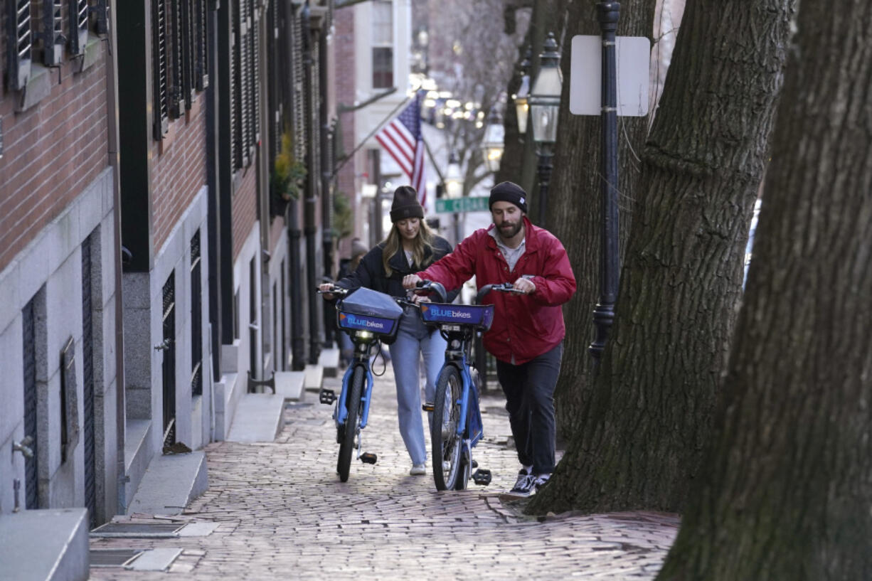 Passers-by walk their bikes up a hill in a residential area near the Statehouse on Beacon Hill, Monday, Feb. 13, 2023, in Boston. For much of the Eastern United States, the winter of 2023 has been a bust. Snow totals are far below average from Boston to Philadelphia in 2023 and warmer temperatures have often resulted in more spring-like days than blizzard-like conditions.