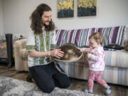 Yevhenii Hornishevskyi, left, lets his daughter Miroslava Hornishevska, 1, play with a tongue drum in their home. Hornishevskyi and his wife handmake and sell tongue drums on Etsy as their main source of income.