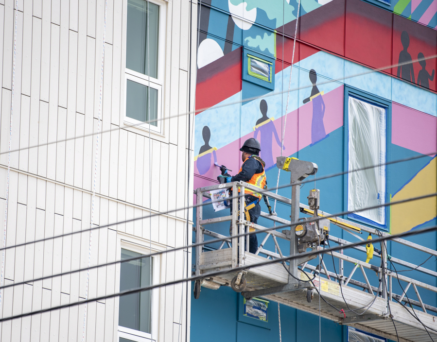 Portland-based artist Christian T?llez works on a mural Tuesday at the Fourth Plain Community Commons building. The mural's design is a tribute to the community's diversity, according to an Instagram post by the city of Vancouver.