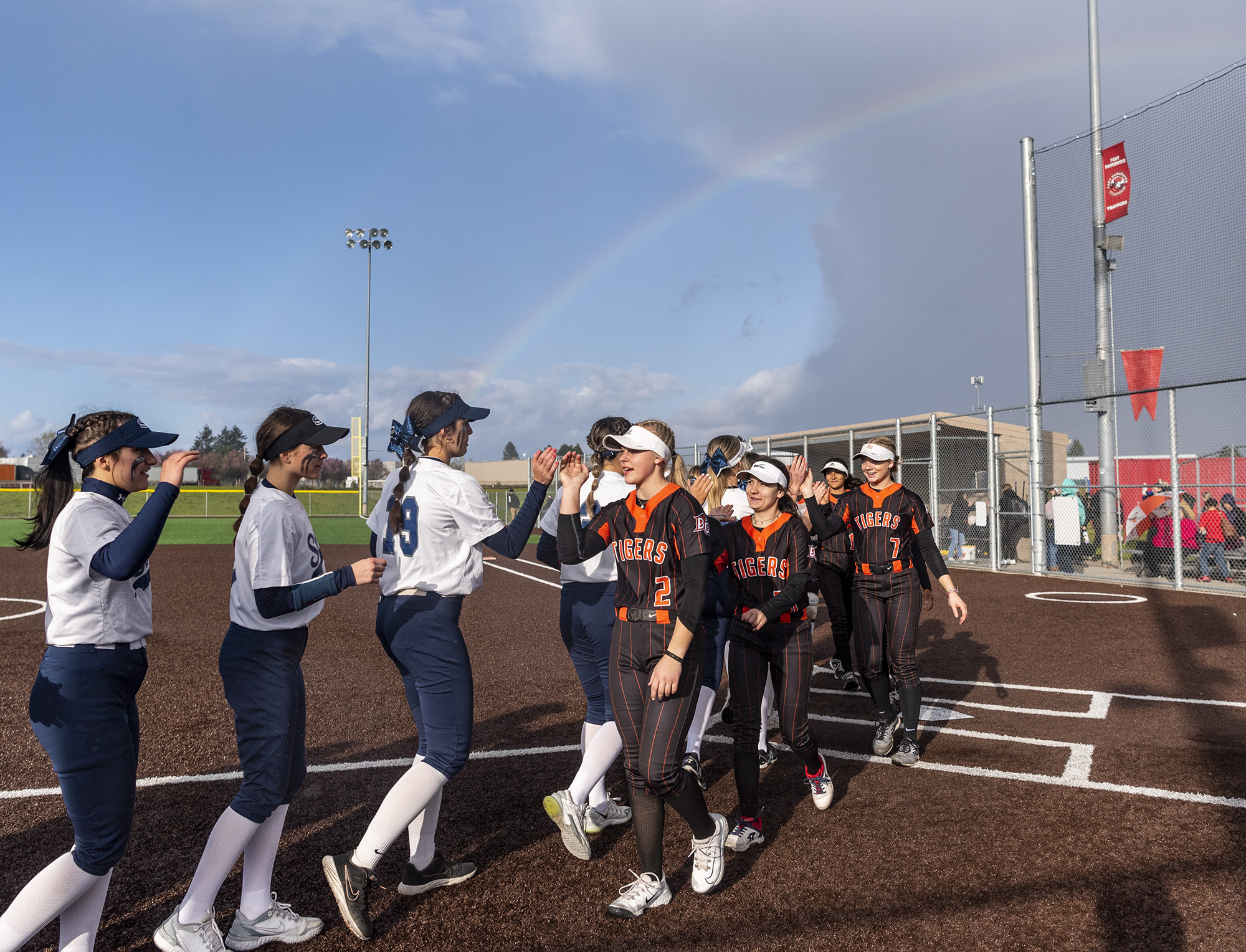 A rainbow hangs above as Skyview and Battle Ground players high five after the game Wednesday, April 12, 2023, after the Storm’s 4-0 win against Battle Ground at Fort Vancouver High School.