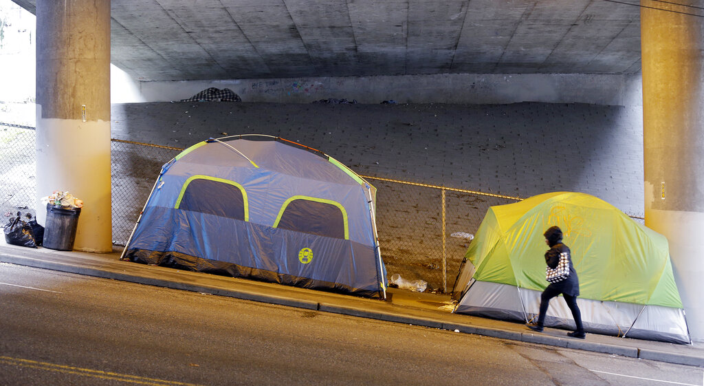 FILE - In this March 8, 2017 file photo, a person walks up a hill next to tents lined up beneath a highway and adjacent to downtown Seattle.   Microsoft pledged $500 million to address homelessness and develop affordable housing in response to the Seattle region's widening affordability gap.  The company plans a news conference, Thursday, Jan. 17, 2019.