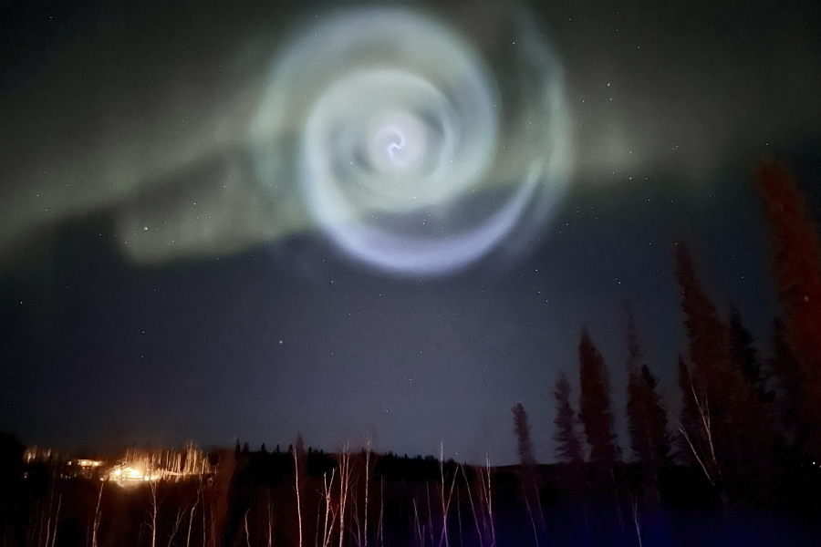 In this photo provided by Christopher Hayden, a light baby blue spiral resembling a galaxy appears amid the aurora for a few minutes in the Alaska skies near Fairbanks, Saturday, April 15, 2023.  The spiral was formed when excess fuel that had been released from a SpaceX rocket that launched from California about three hours earlier turned to ice, and then the water vapor reflected the sunlight in the upper atmosphere.