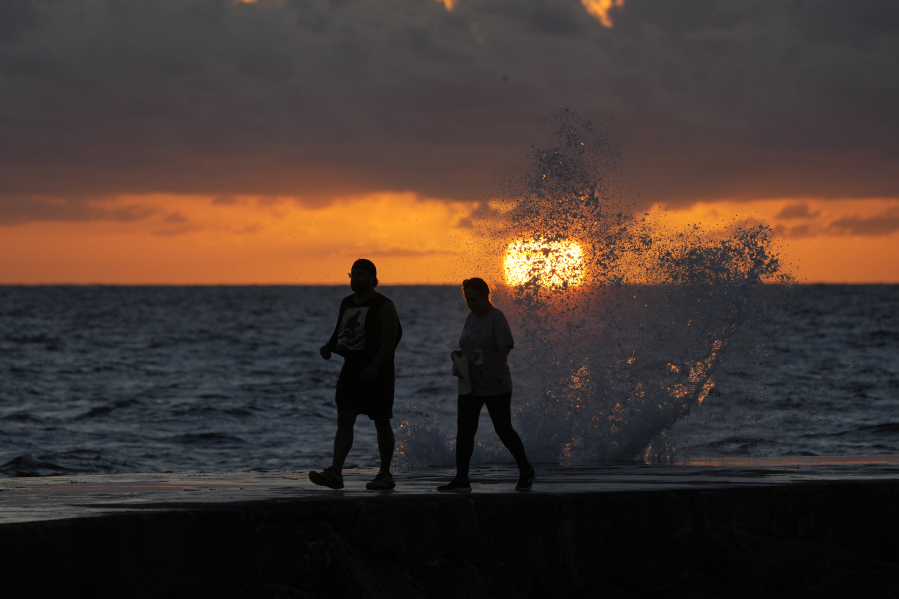 FILE - The sun rises above the Atlantic Ocean as waves crash near beach goers walking along a jetty, Dec. 7, 2022, in Bal Harbour, Fla. The world's oceans have suddenly spiked much hotter and well above record levels, with scientists trying to figure out what it means and whether it forecasts a surge in atmospheric warming.