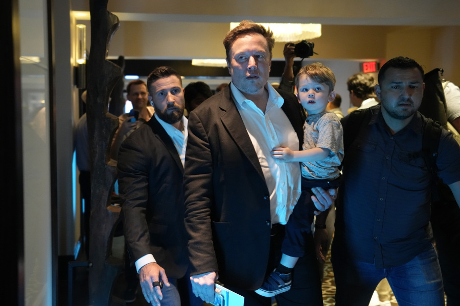 Twitter CEO Elon Musk, center, carries his child as he leaves after speaking at the POSSIBLE marketing conference, Tuesday, April 18, 2023, in Miami Beach, Fla.